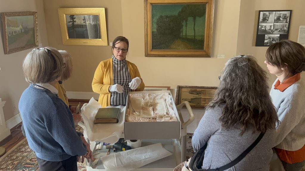 three people gathered around a museum curator wearing gloves and showing a museum material