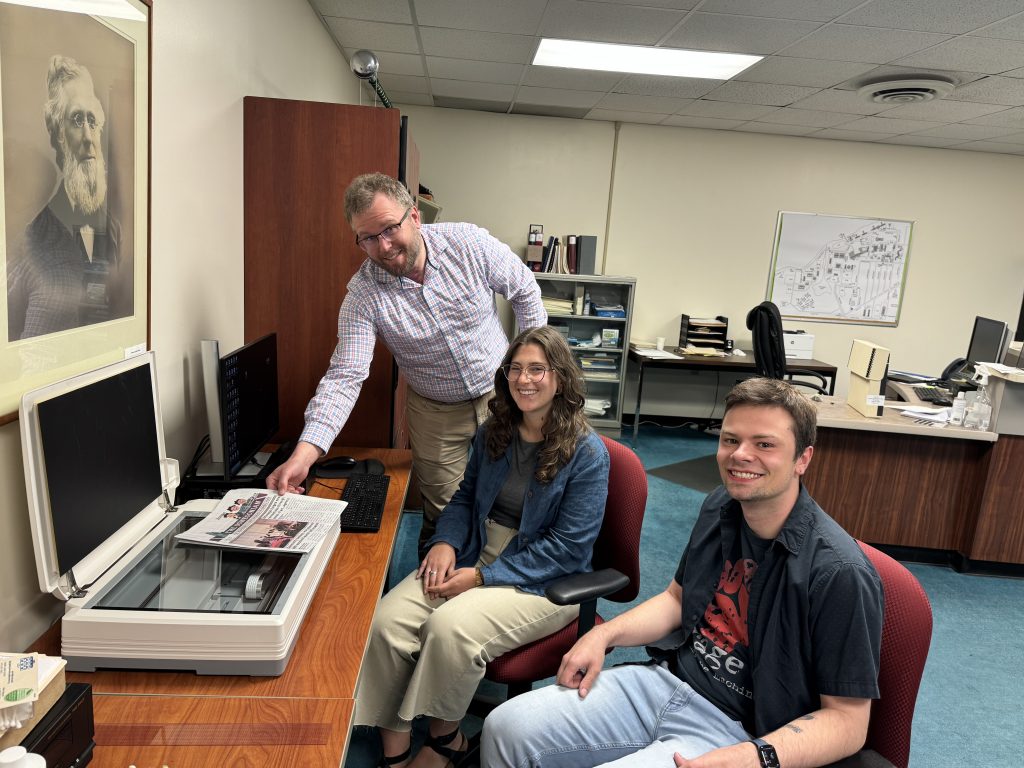 Three people gathered around a digital scanner