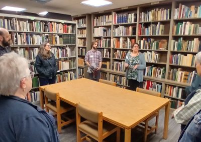 Group of people standing around a large table in a room filled with shelves of books.