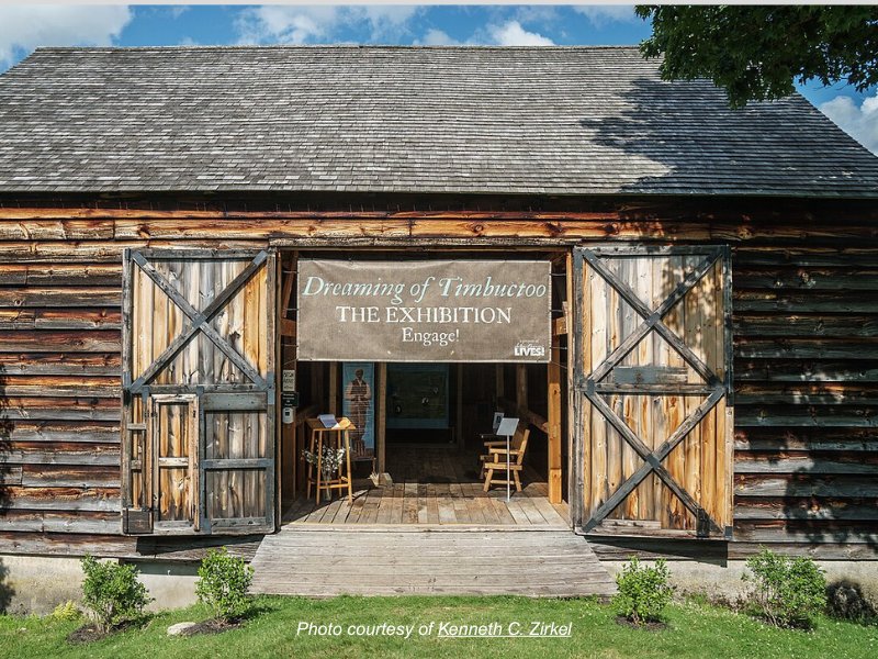 Wooden barn with doors open to reveal banner reading "Dreaming of Timbuctoo: the Exhibition"
